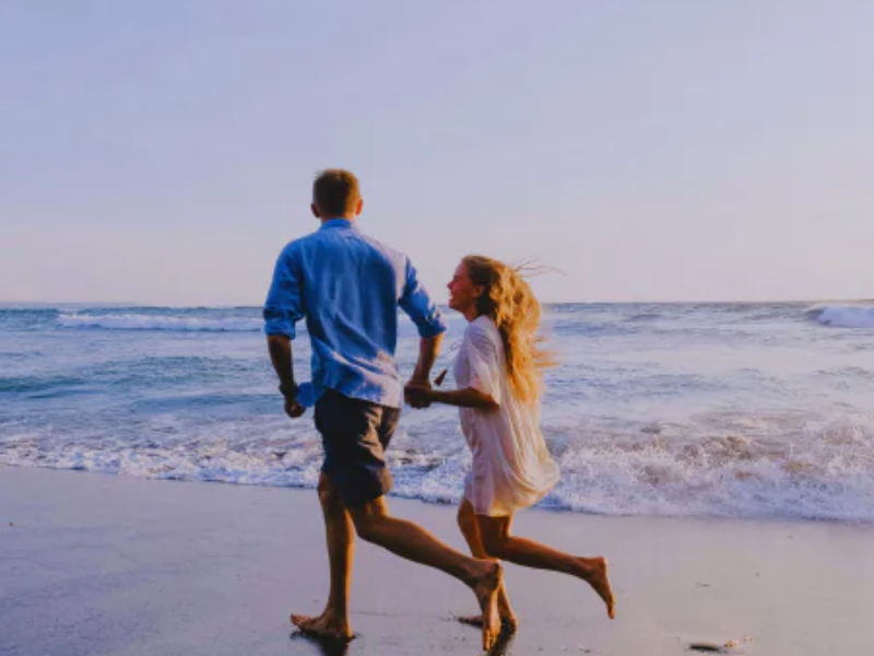 man and women running on the beach with ocean in the background